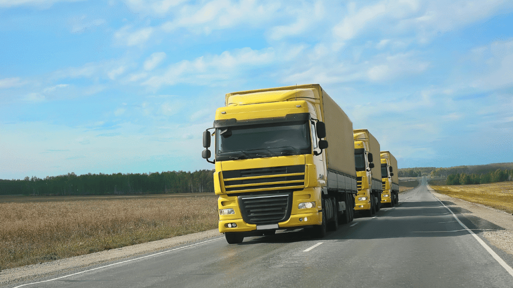Three yellow freight trucks driving in a line on an open highway, representing fuel cards and route optimization for better fleet fuel savings and efficient route planning.